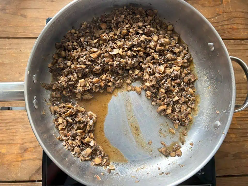 Diced mushrooms cooking in pan with little liquid.