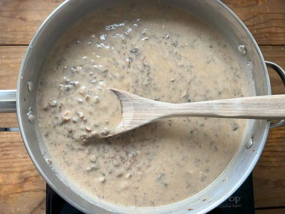 Vegan cream of mushroom soup in a large pan with a mixing spoon on wood table.