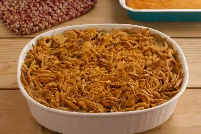 Vegan green bean casserole in white dish on wood table with sides in the background.