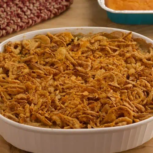 Vegan green bean casserole in white dish on wood table with sides in the background.