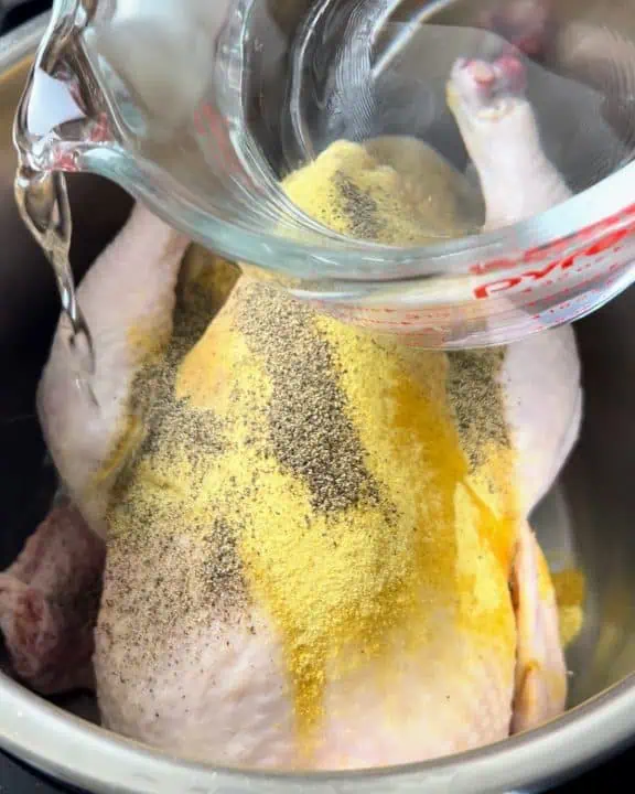 Pouring water over whole chicken seasoned with Adobo and black pepper.