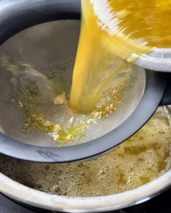 Passing chicken broth through fine mesh strainer into Instant Pot.