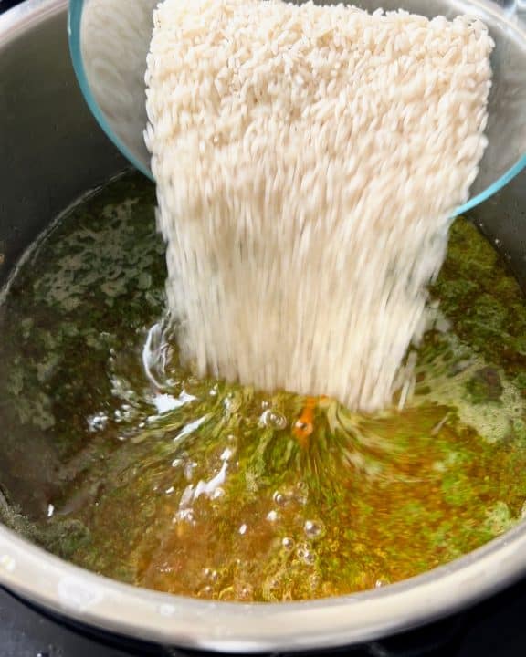 Pouring uncooked rice into chicken broth with sofrito.