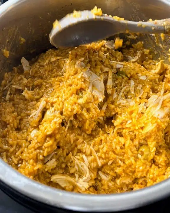 Stirring chicken and rice with large spoon inside Instant Pot.