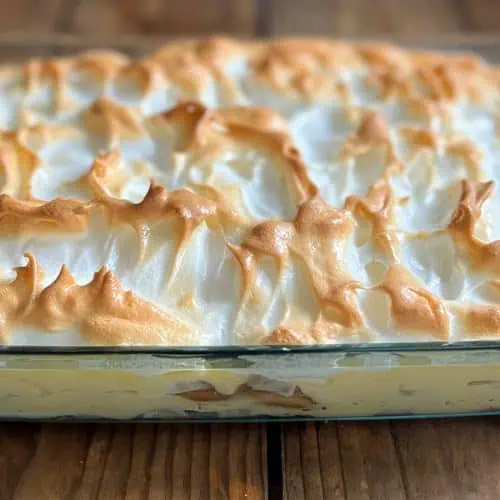 Southern banana pudding with meringue topping in pyrex dish on wood table.