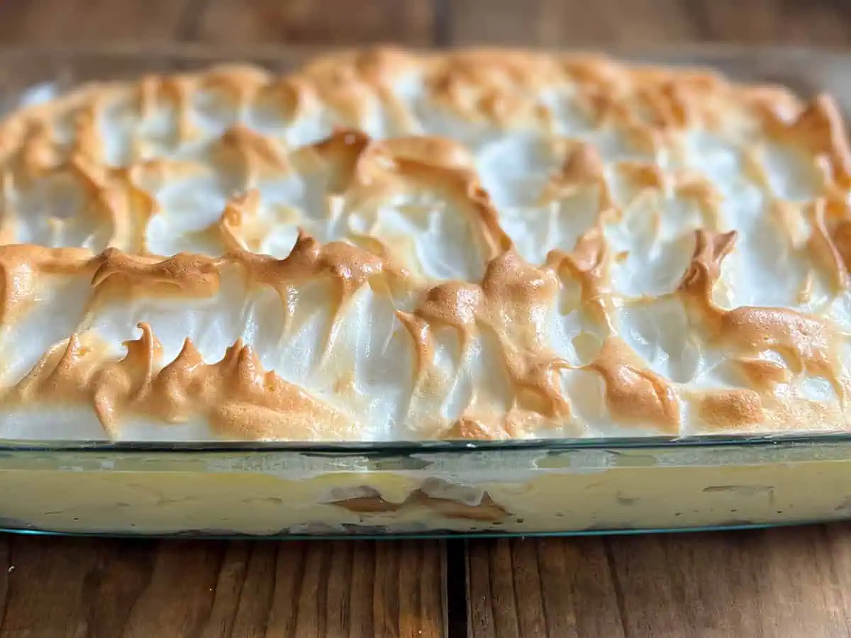 Southern banana pudding with meringue topping in pyrex dish on wood table.