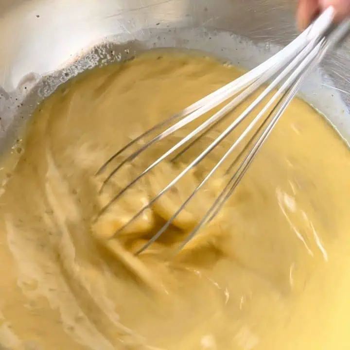 A metal whisk stirs through a bowl of thick egg custard.