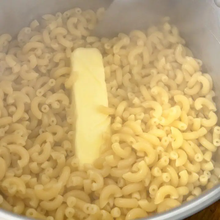 A pot filled with macaroni and butter, actively being stirred to melt the butter.