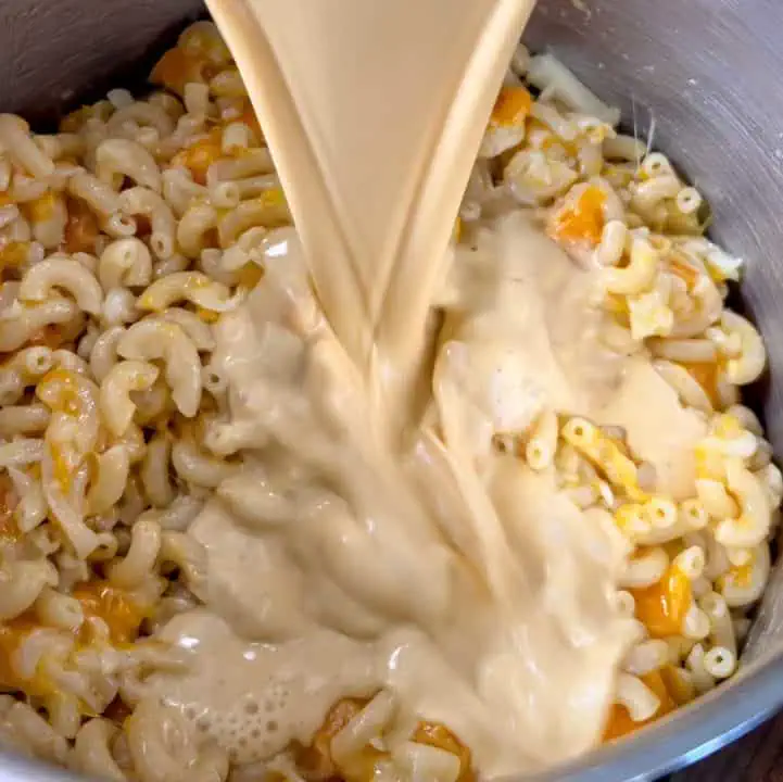 Pouring egg custard into a pot filled with macaroni and cubed cheddar cheese.