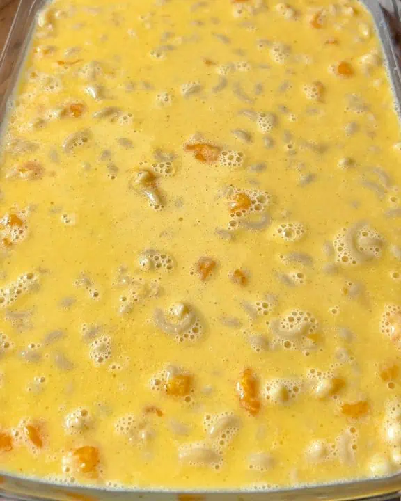 A casserole dish filled with macaroni, cubes of cheddar cheese, and egg custard.