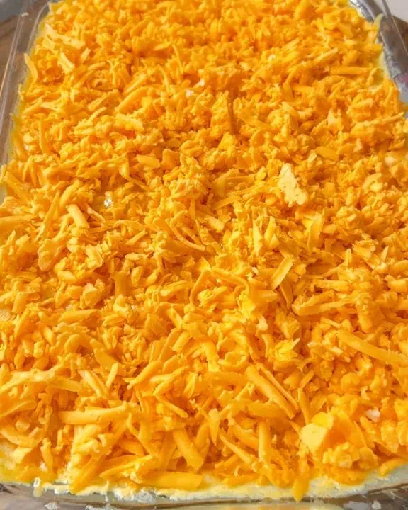 A casserole dish filled to the top and topped with shredded chaddar cheese.