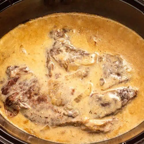 A slow cooker filled with tender chuck roast immersed in rich, savory gravy.