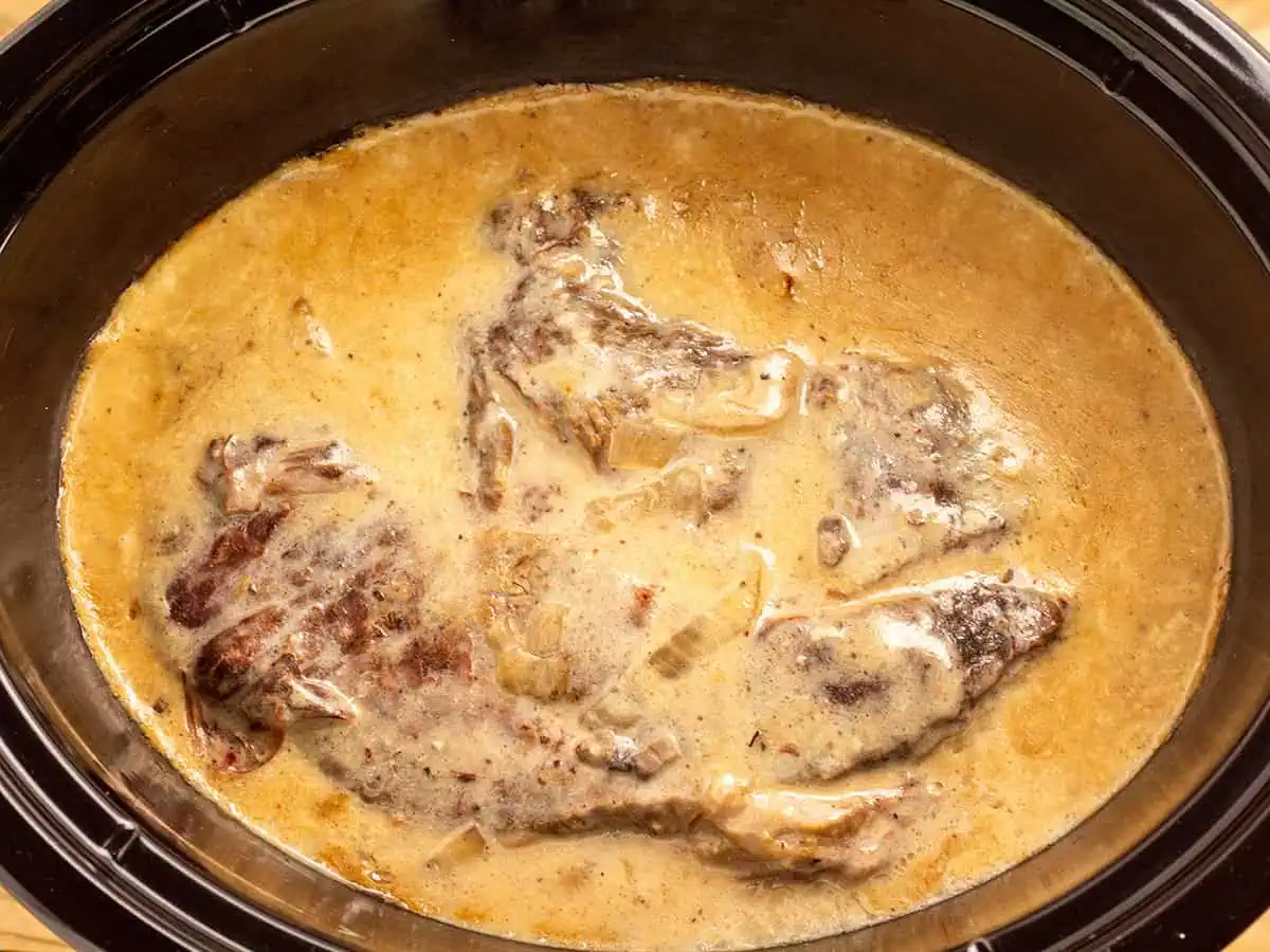 A slow cooker filled with tender chuck roast immersed in rich, savory gravy.