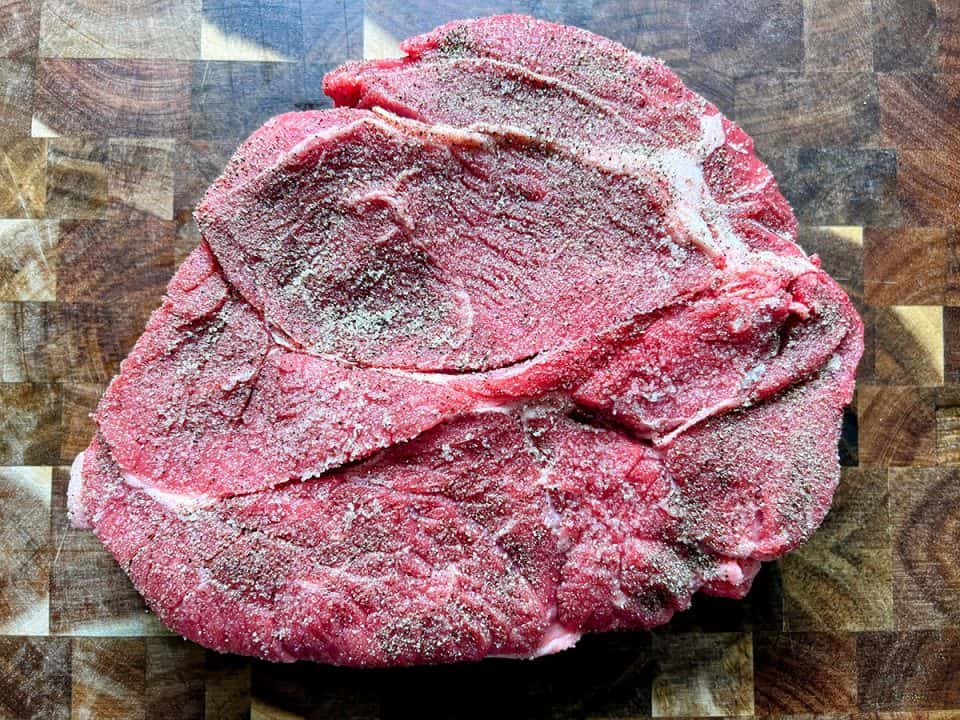 An uncooked, seasoned chuck roast on a wood cutting board.