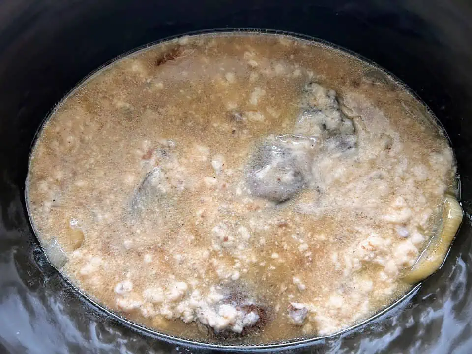 A Crock Pot with a chuck roast and sliced onions topped with cream of mushroom soup.