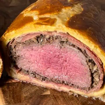 Beef Wellington, partially sliced, showing the inside layers of filet mignon, mushrooms, prosciutto, crepe, and crispy puff pastry.