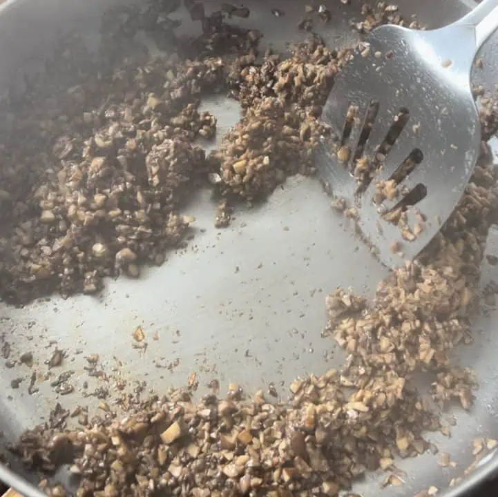 A pan filled with cooked diced mushrooms being mixed with a spatula.