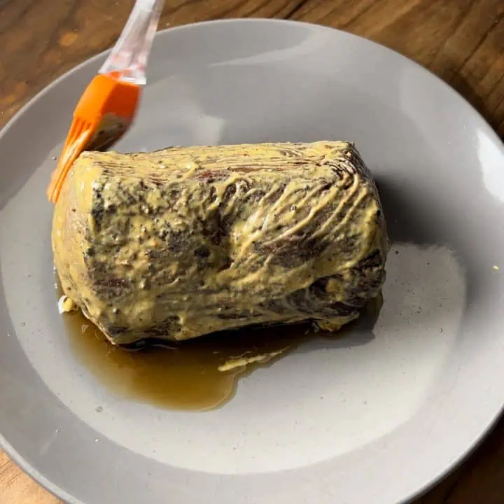 A chateaubriand on a gray plate being basted with Dijon mustard.