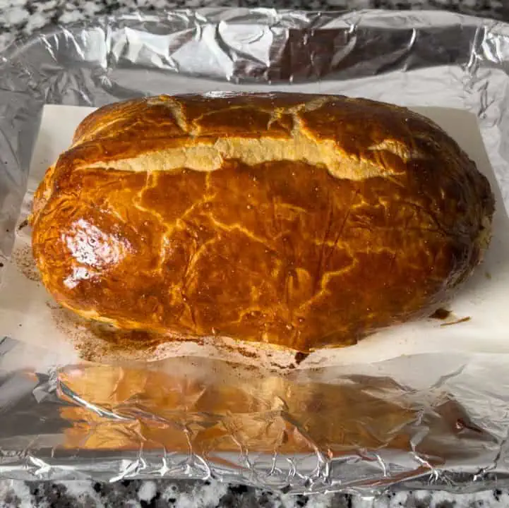 A whole cooked Beef Wellington on a tray with aluminum foil and parchment paper.