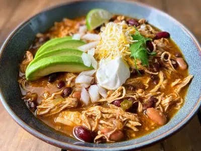 A hearty bowl of Instant Pot chicken chili, featuring tender chicken and beans, topped with cheese, sour cream, and avocado.