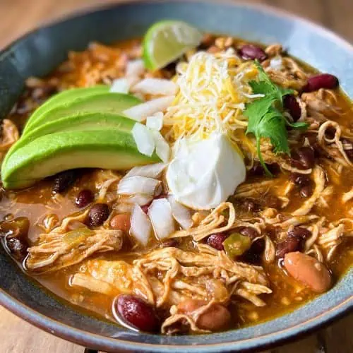 A hearty bowl of Instant Pot chicken chili, featuring tender chicken and beans, topped with cheese, sour cream, and avocado.