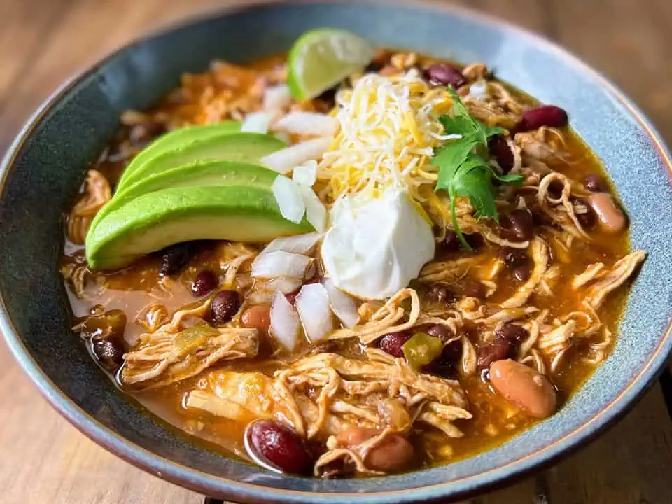 A hearty bowl of Instant Pot chicken chili, featuring tender chicken and beans, topped with cheese, sour cream, and avocado.