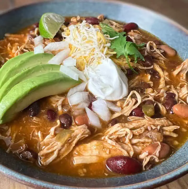 A hearty bowl of Instant Pot chicken chili, featuring tender chicken and beans, topped with cheese, sour cream, and avocado.