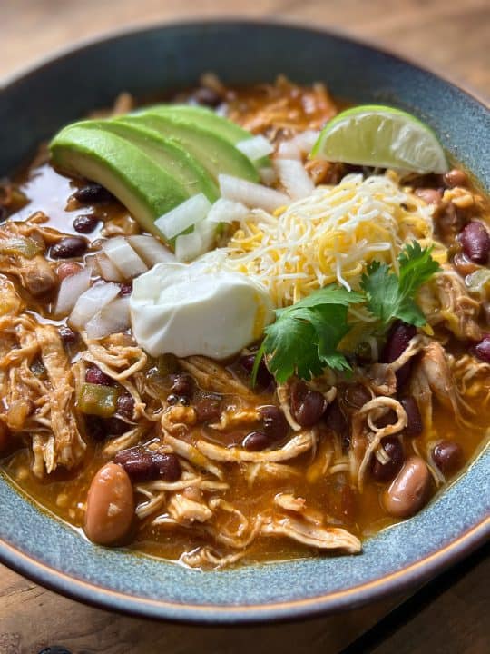 A hearty bowl of Instant Pot chicken chili, featuring tender chicken and beans, topped with cheese, sour cream, and avocado.