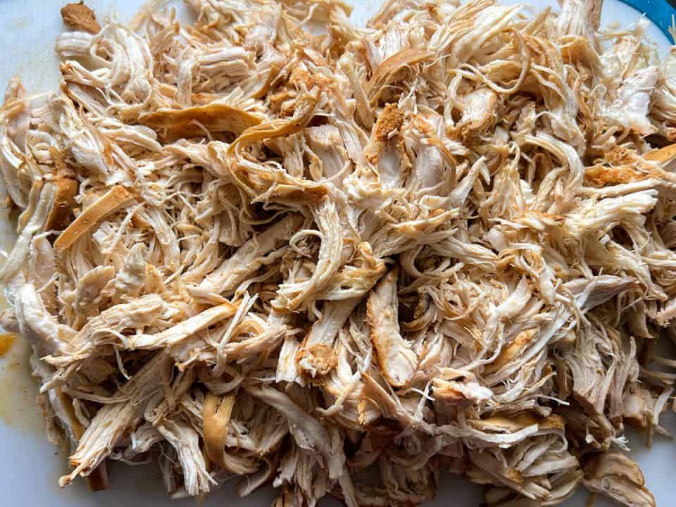 Shredded chicken on a white cutting board.