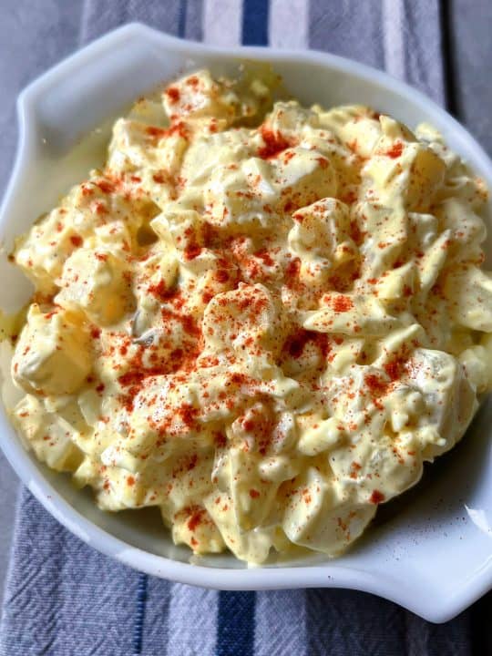 Instant Pot potato salad toped with paprika in a white bowl with a gray and blue background.