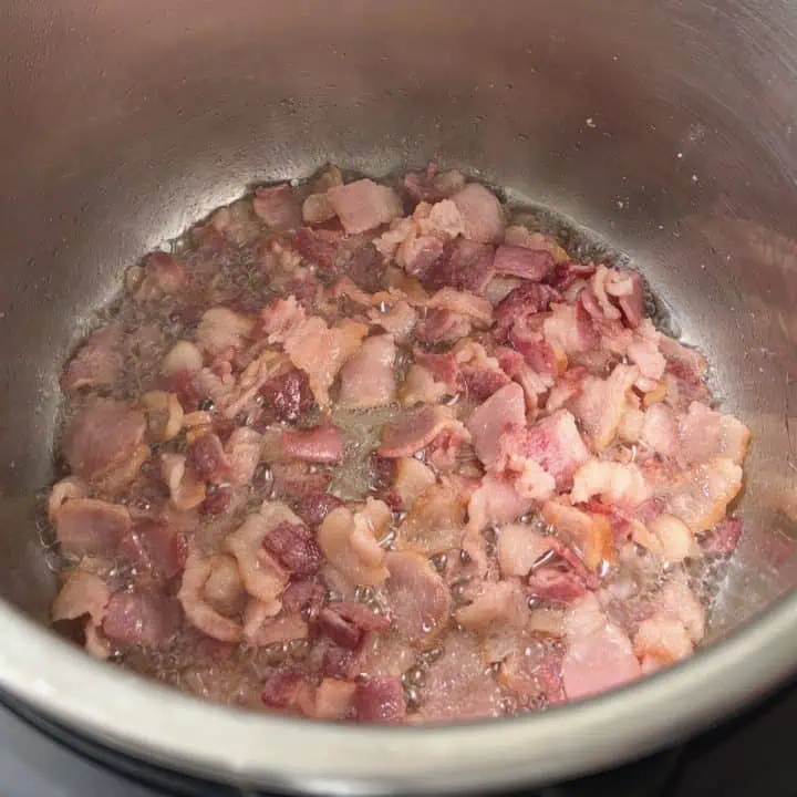 Chopped bacon pieces sauteing in a pressure cooker.