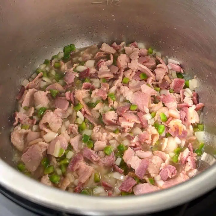 Chopped bacon cooking in a pressure cooker with green peppers and onions.