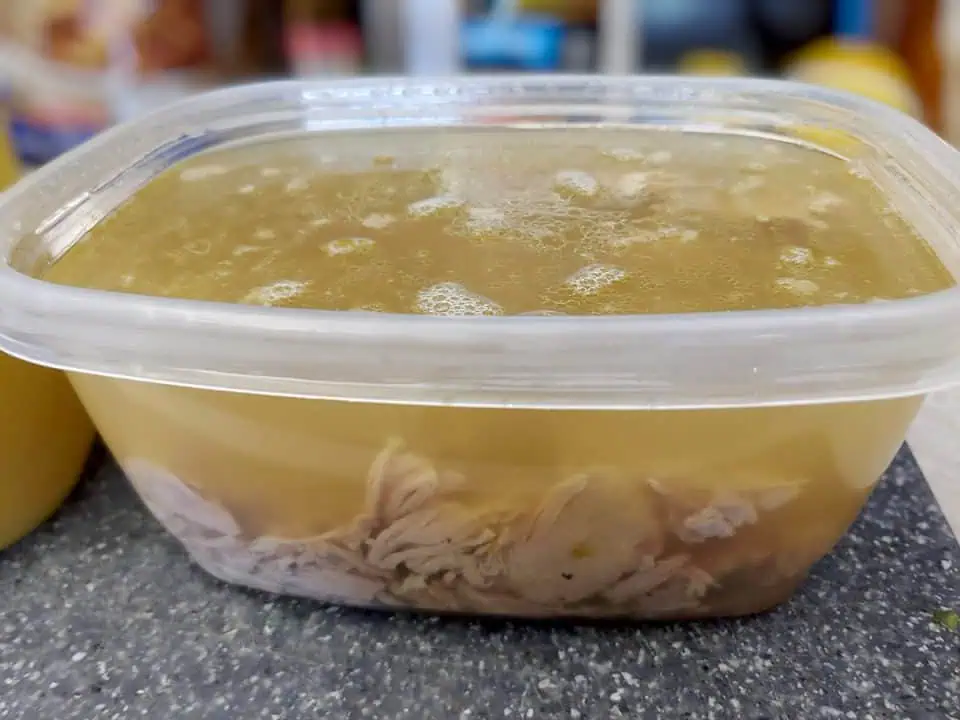 Shredded turkey and stock in plastic container.