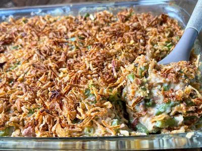 A casserole dish filled with green beans topped with crispy onions, being scooped with a serving spoon.