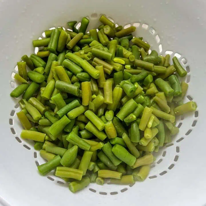 Blanched green beans draining in a white colander.