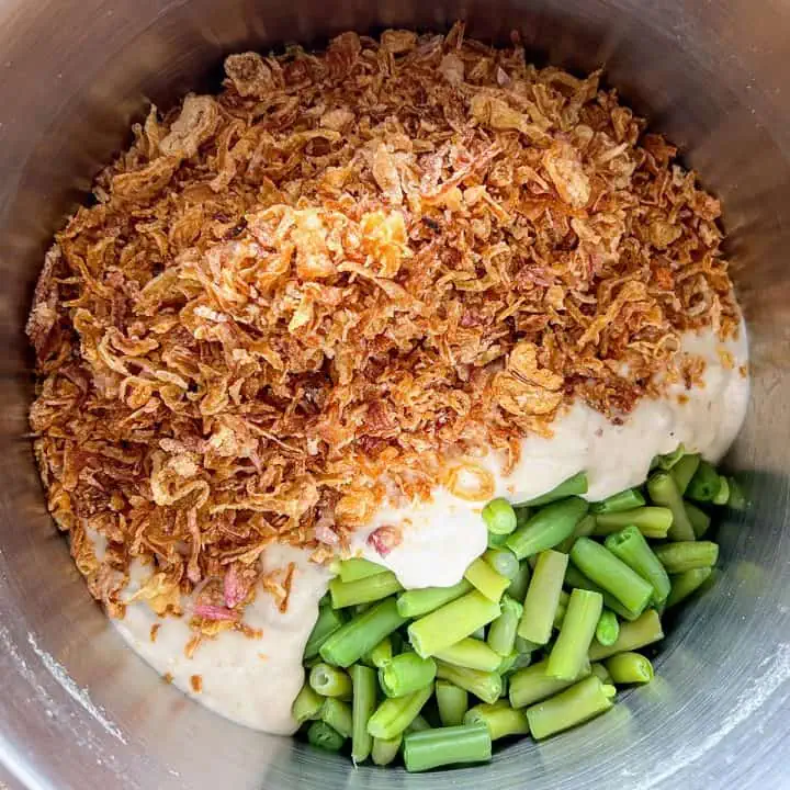 A stainless steel pot filled with fresh green beans topped with creamy soup and crispy onions.