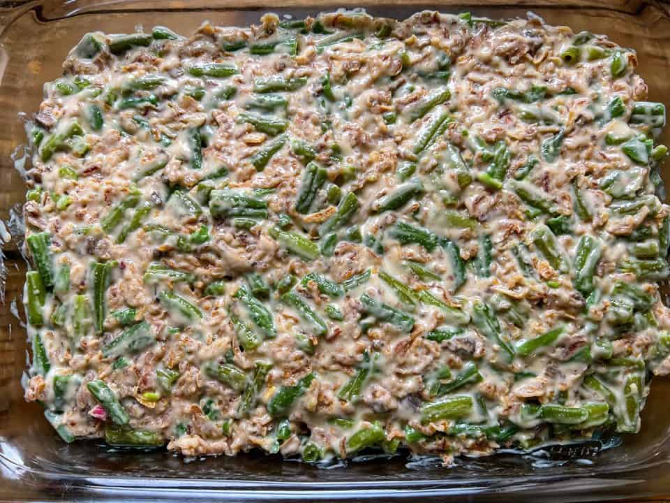 A casserole dish containing a mix of green beans, cream of mushroom soup, and crispy fried onions.