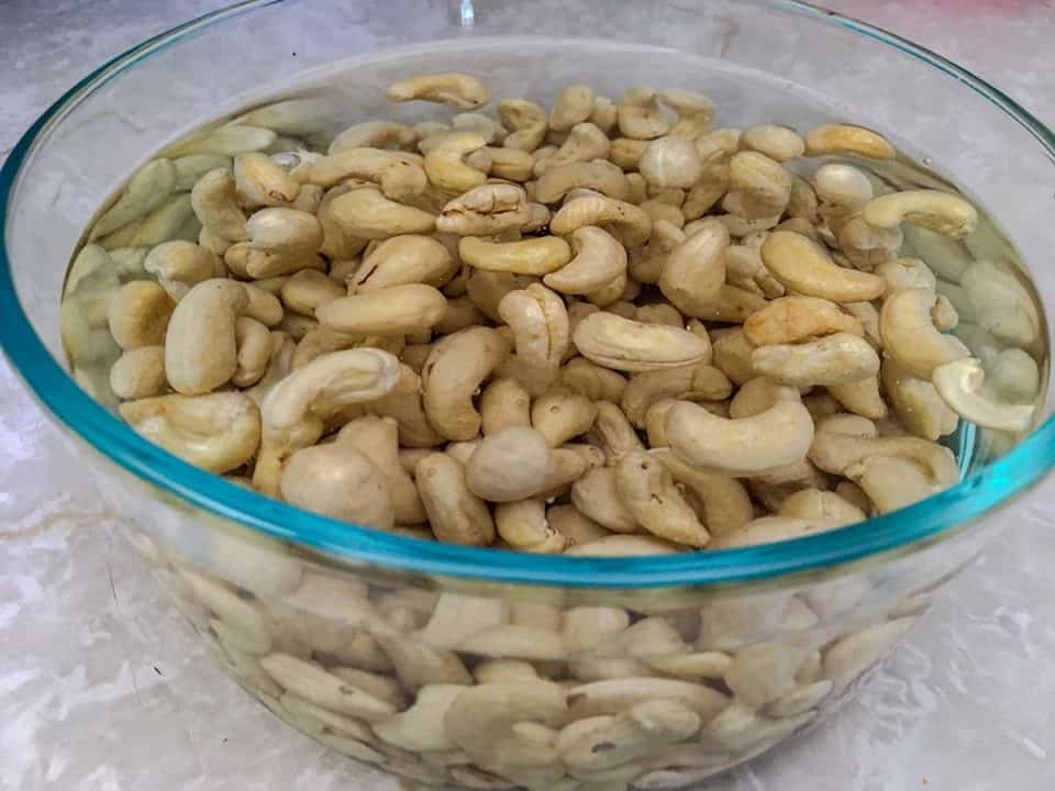A glass bowl filled with raw cashews soaking in water.