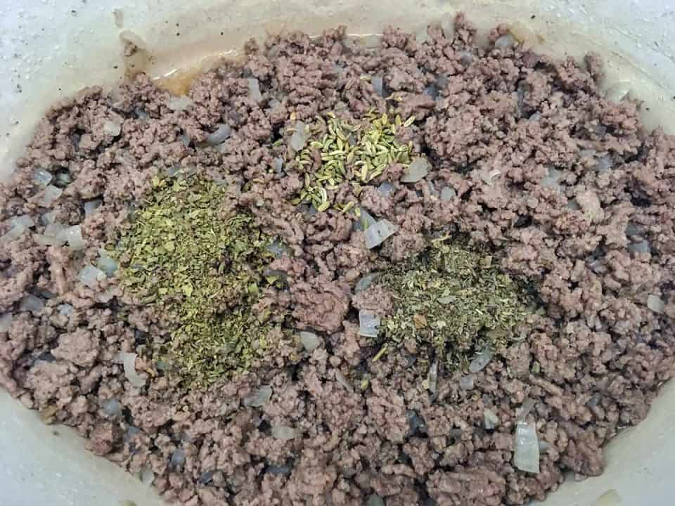 Cooked ground beef in a Dutch oven topped with dried herbs.