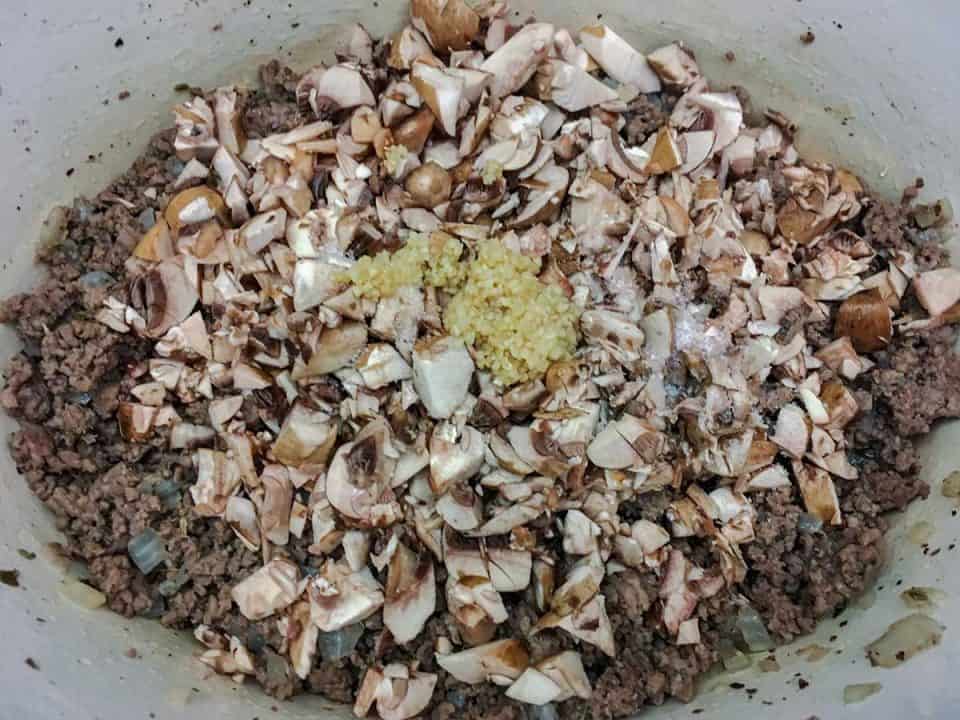Browned ground beef topped with diced mushrooms and minced garlic in a Dutch oven.