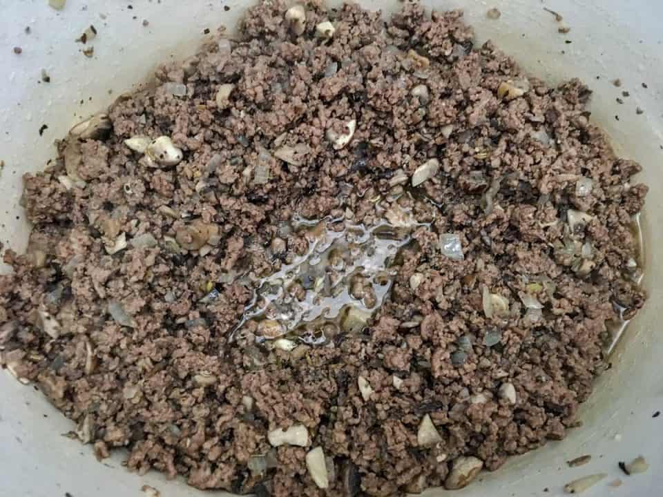 Browned ground beef and mushrooms cooking in a Dutch oven.