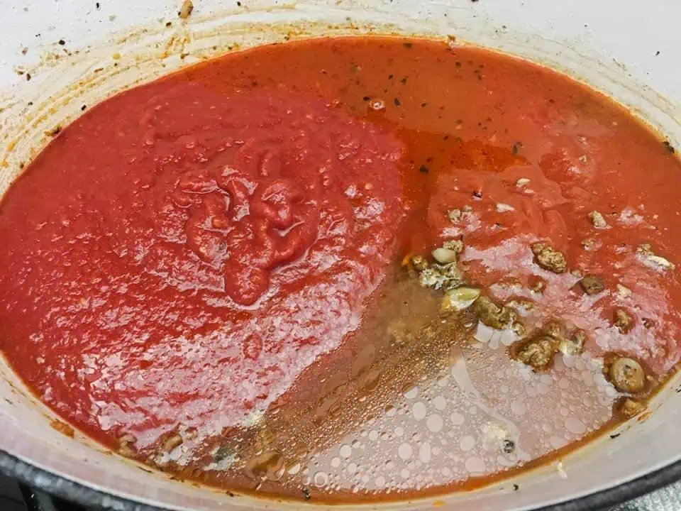 Dutch oven filled with ground beef and mushrooms, topped with crushed tomatoes and water.