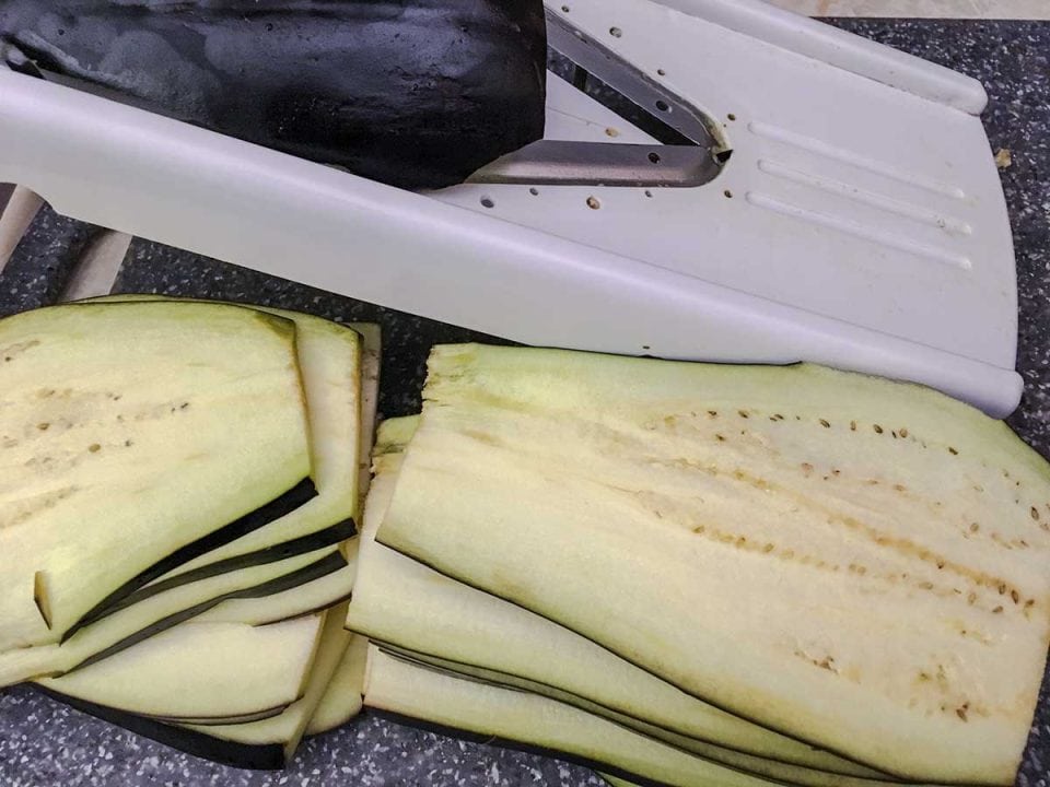Slicing globe eggplant with a mandolin on a cutting board.