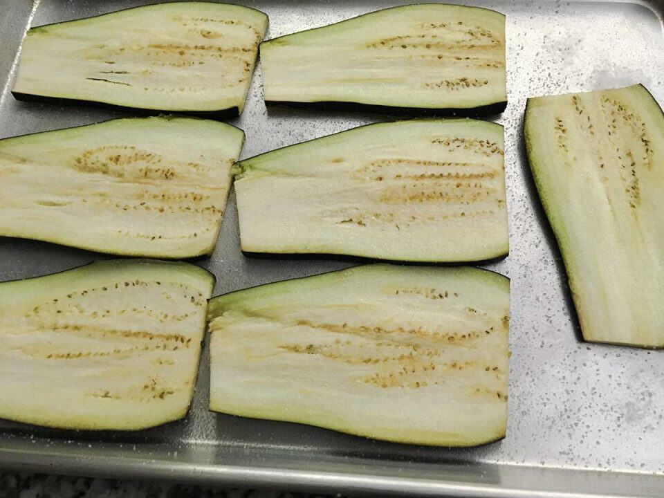Slices of eggplant on a baking sheet seasoned with salt.