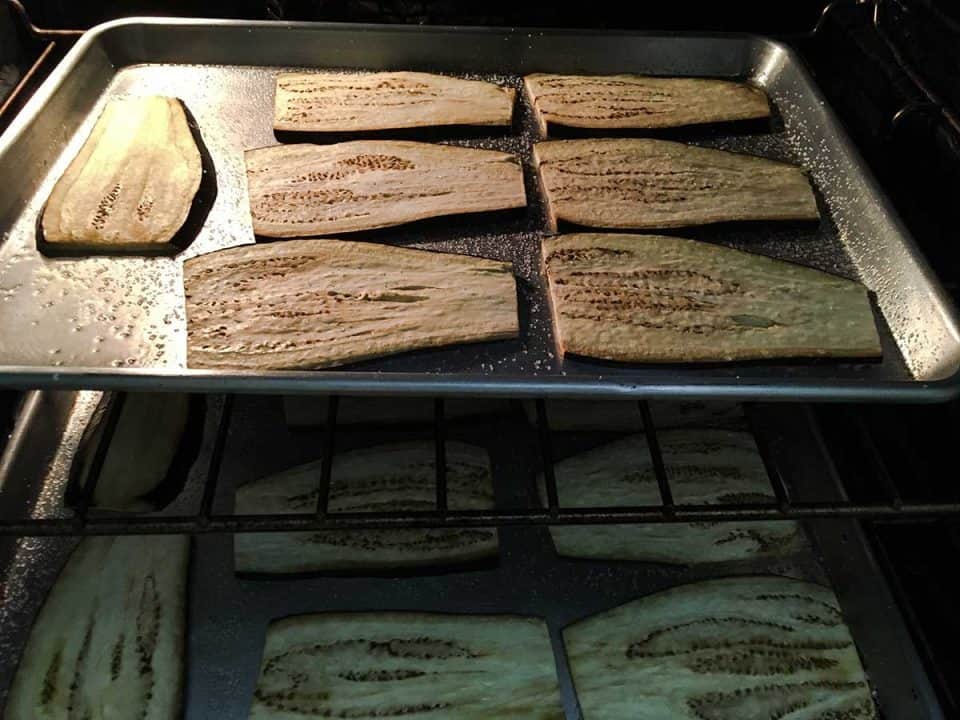 Two baking traying in the oven roasting slices of eggplant.