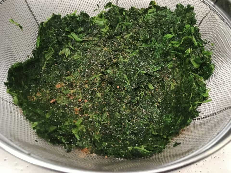 Frozen spinach draining on a wire colander, topped with grated nutmeg.