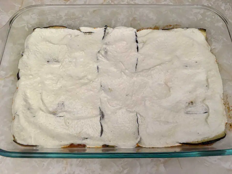 A casserole dish with layers of lasagna, topped with cashew cream.