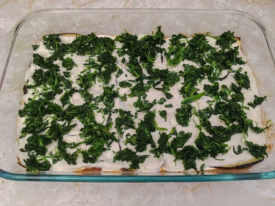 A casserole dish with a layer of cashew cream topped with frozen spinach.
