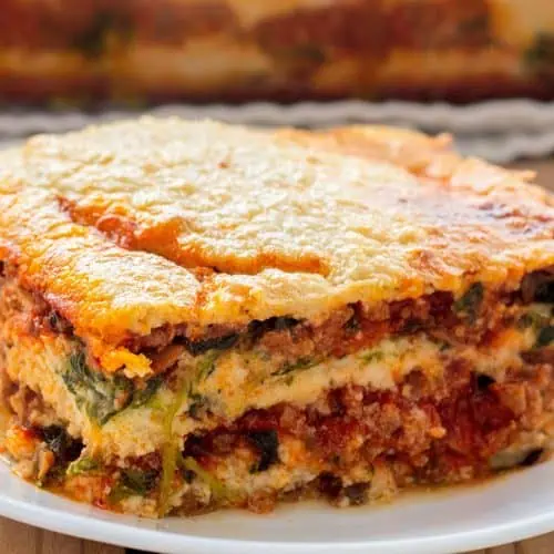 A slice of Whole30 lasagna on a white plate showing layers of eggplant noodles, rich meat sauce, and golden cashew cream.