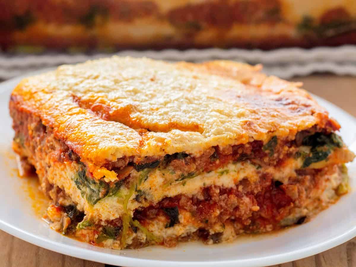 A slice of Whole30 lasagna on a white plate showing layers of eggplant noodles, rich meat sauce, and golden cashew cream.